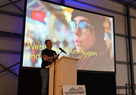 Ein Mann steht vor einer bunten Leindwand und hält einen Vortrag über KI und Tourismus.