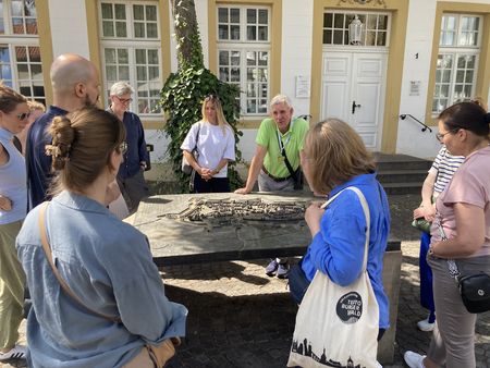 Ein Gästeführer und eine Gruppe betrachten ein Stadtmodell.