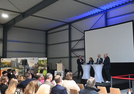 Zuschauer sitzen in Reihen vor einer Bühne; auf der Bühne befinden sich fünf Personen an Stehtischen im Gespräch