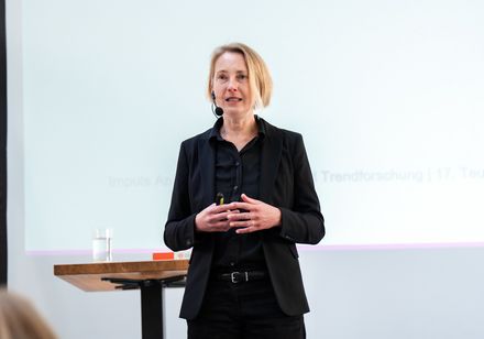 Eine Frau steht auf einer Bühne und hält einen Vortrag.