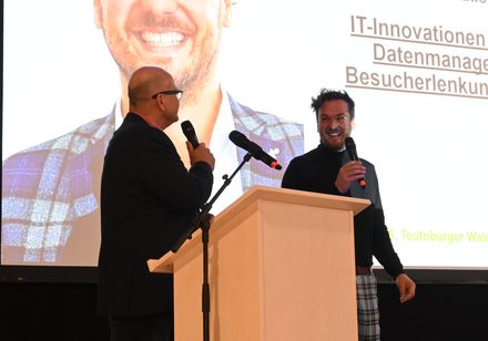 Auf einer Bühne stehen zwei Personen vor einer Leinwand.