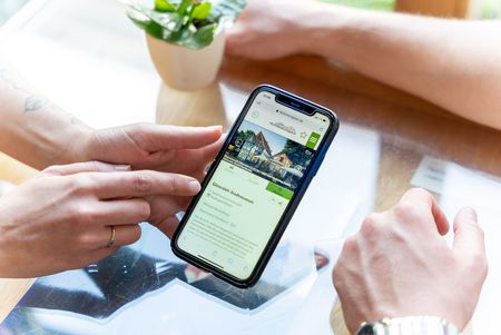 Das Foto zeigt Hände, die ein Smartphone bedienen, auf dem die Plattform Teuto-Navigator eingeblendet ist.