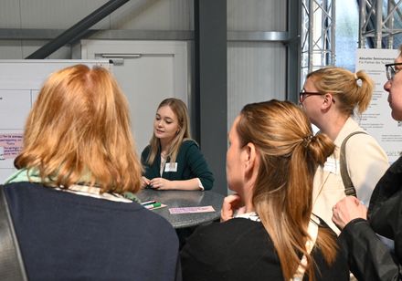 Eine Gruppe von Menschen steht an einem Stehtisch zusammen; die Gruppe ist in eine Diskussion vertieft.