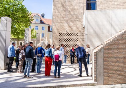 Geführter Rundgang einer Besuchergruppe durch einen modernen Innenhof mit Backsteinarchitektur.