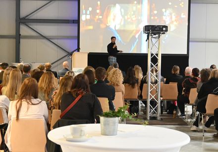Ein Referent steht auf einer Bühne und hält einen Vortrag.