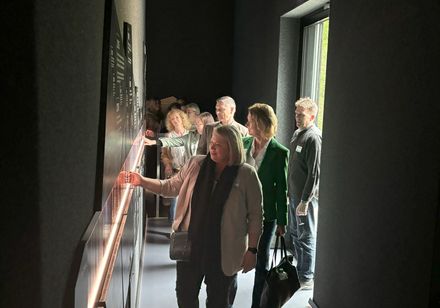 Eine Gruppe von Menschen betrachtet in einem Museum eine Informationstafel an der Wand.