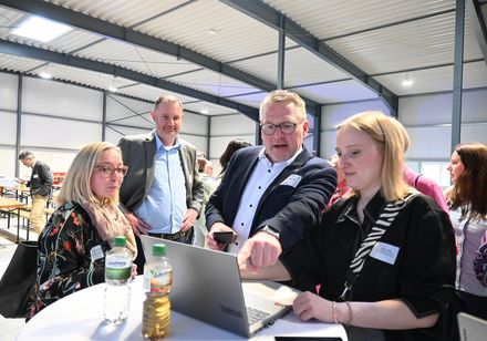 Eine Gruppe von Menschen steht vor einem aufgeklappten Laptop.