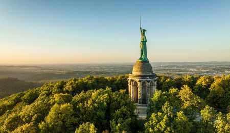 Hermann, der Cherusker, als Statue auf einer dicht bewaldeten Erhöhung.