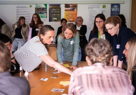 In einem Workshop betrachtet eine Gruppe von Teilnehmenden Materialien auf einem Tisch.