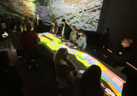 In einem verunkelten Raum betrachten Museumsbesucher eine hell erleuchtete Informationstafel.