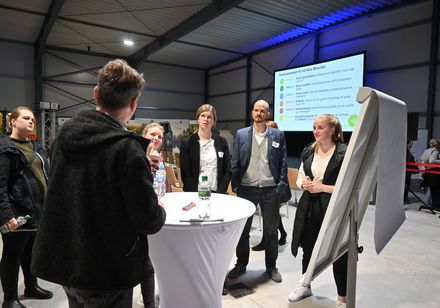 Eine Gruppe von Menschen steht an einem Stehtisch und einem Flipchart.