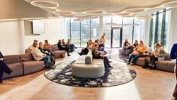 Personengruppe sitzt in einem modernen, lichtdurchfluteten Foyer auf Sofas und unterhält sich bei Kaffee und Gebäck.