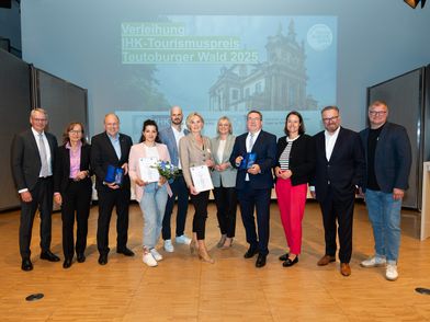 Auf dem Bild sind elf Personen, Männer und Frauen, zu sehen, die lächelnd in die Kamera Blicken und zum Teil einen Preis in der Hand halten. Sie befinden sich auf der Bühne, im Hintergrund sieht man die Folie einer Präsentation.