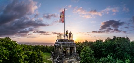 Zwei Personen stehen auf dem Bismarckturm in Herford, die Abendsonne sinkt am Horizont nieder.