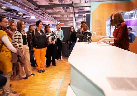 Eine Gruppe von Menschen steht in einem Museum vor einer Ausstellungsfläche.