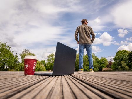 Mann steht auf einem Holzsteg, im Vordergrund Laptop und Kaffeebecher
