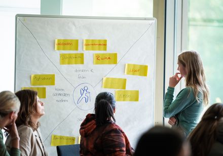 In einer Workshopatmosphäre steht eine Frau vor einer Pinnwand.