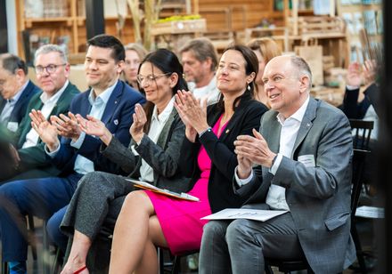 Fünf Personen sitzen auf einem Event in der ersten Reihe und klatschen.