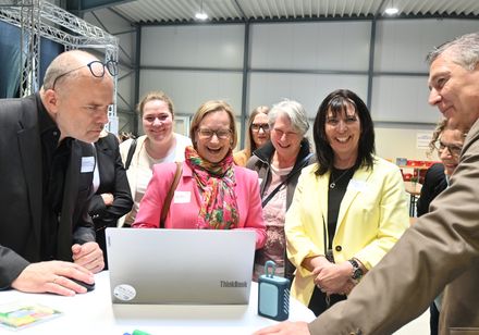 Eine Gruppe von Menschen steht vor einem aufgeklappten Laptop.