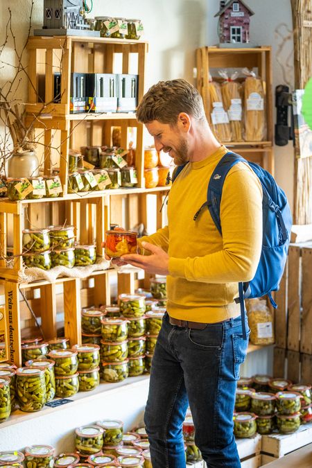 Ein Mann mit Rucksack steht vor einem Regal mit Essiggurken im Geschäft von Bauer Peine in Bad Driburg und begutachtet das Sortiment